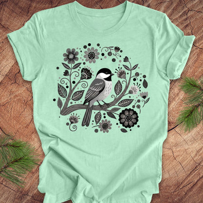 Mint green t-shirt with a bird and floral design on a wooden surface