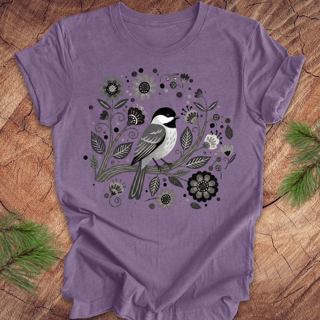 Purple t-shirt with a chickadee bird and floral design on a wooden surface