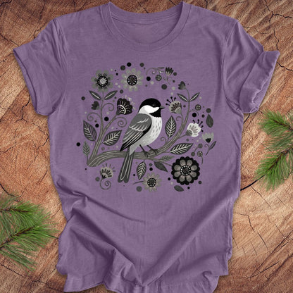 Purple t-shirt with a chickadee bird and floral design on a wooden surface