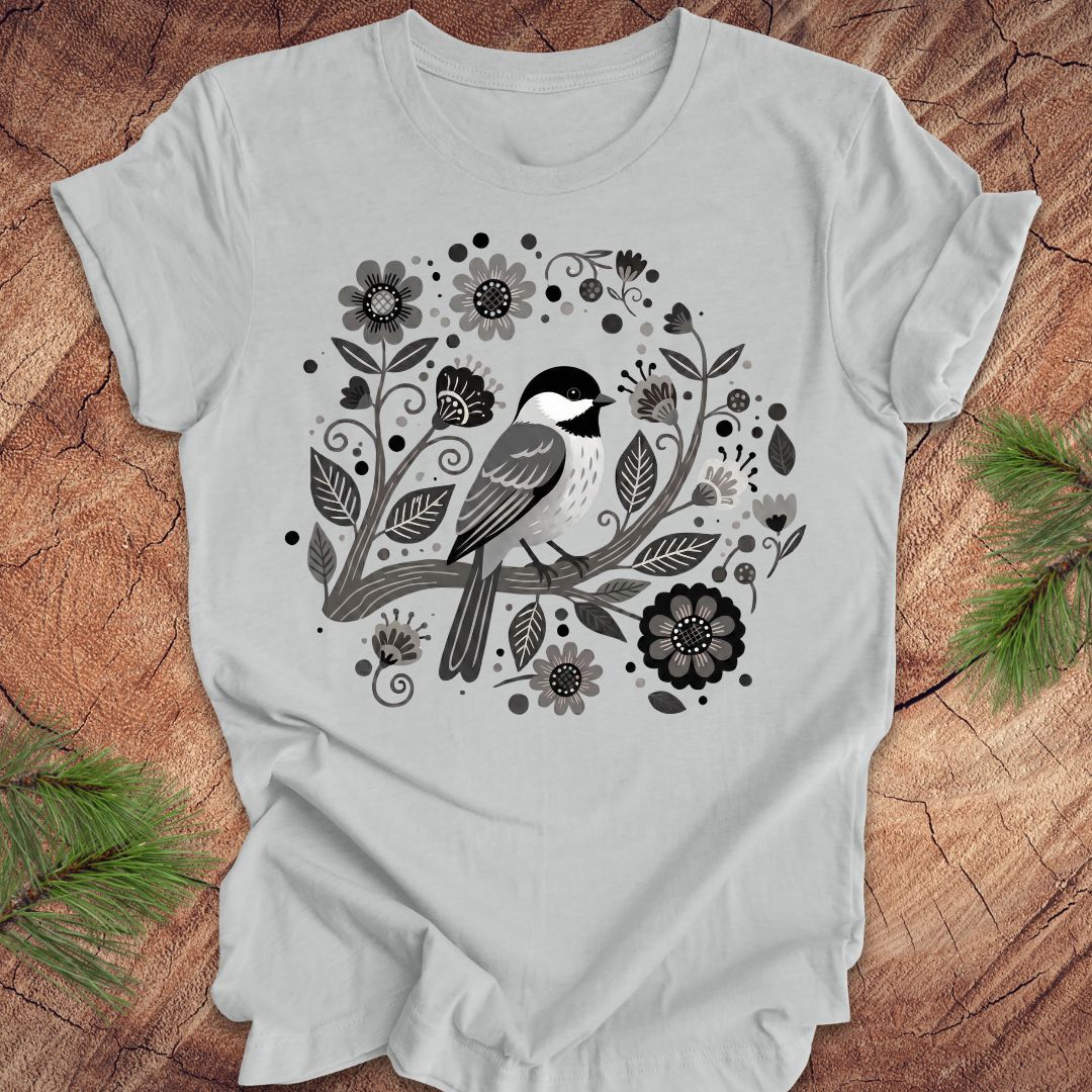 Gray t-shirt with a chickadee bird and floral design on a wooden surface