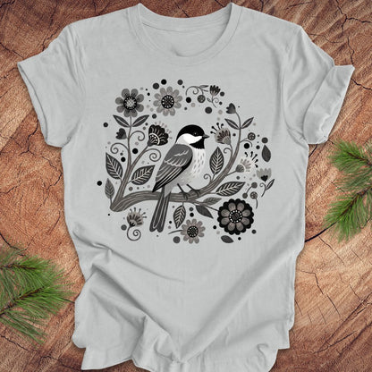 Gray t-shirt with a chickadee bird and floral design on a wooden surface