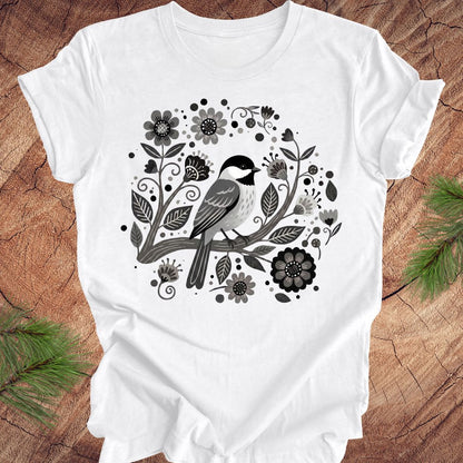White t-shirt with a chickadee bird and floral design on a wooden surface