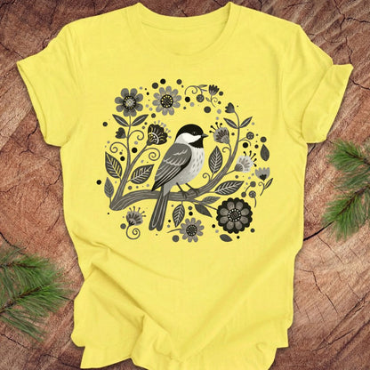 Yellow t-shirt with a chickadee bird and floral design on a wooden surface