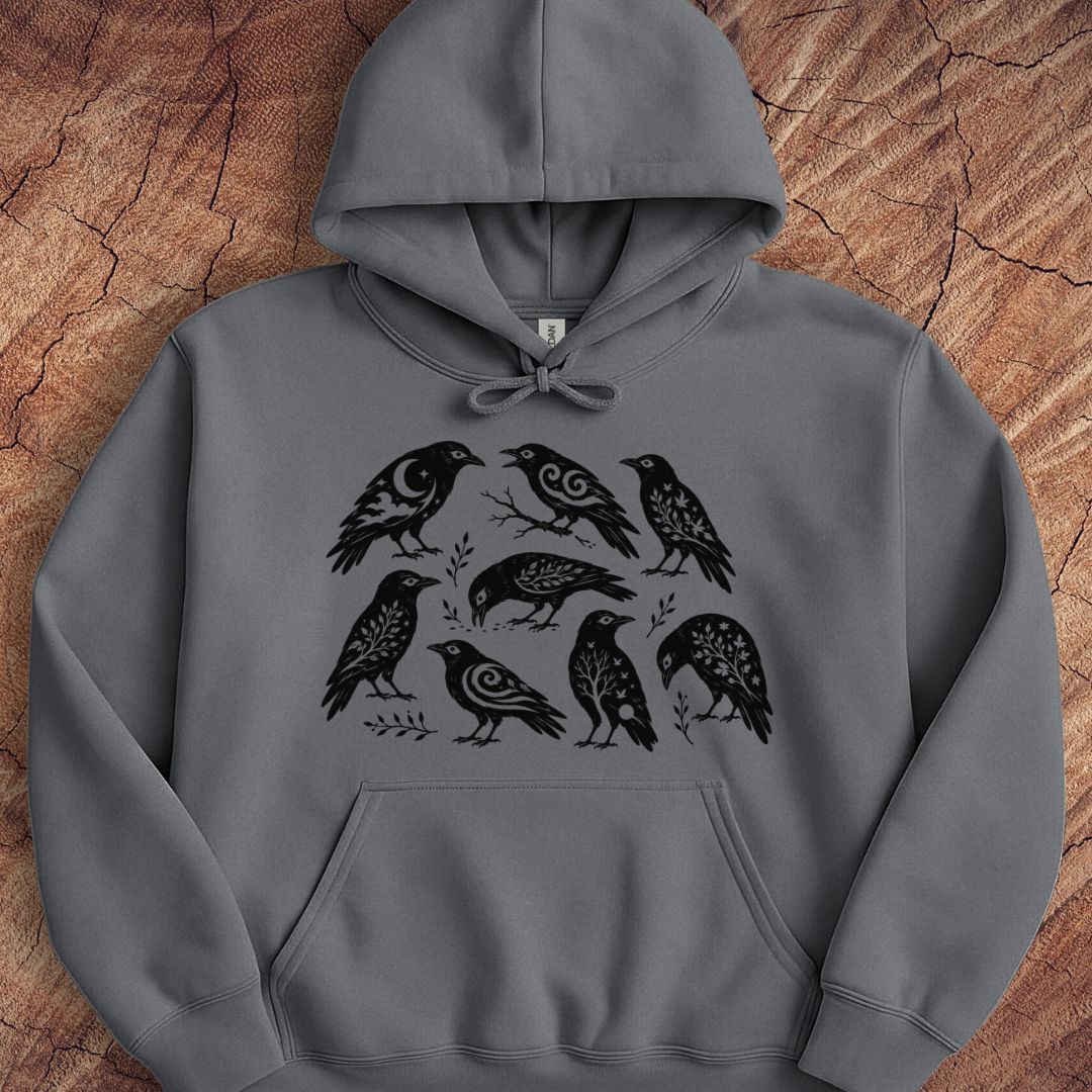 A dark gray pullover hoodie featuring a black graphic print of nine birds arranged in a circle, laid flat on a textured brown wood background.