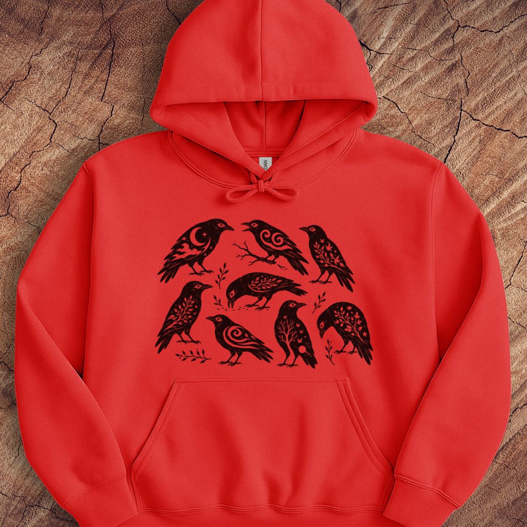 A bright red pullover hoodie with a black graphic print of seven stylized birds arranged in a circle on the front, displayed flat on a textured wood background.