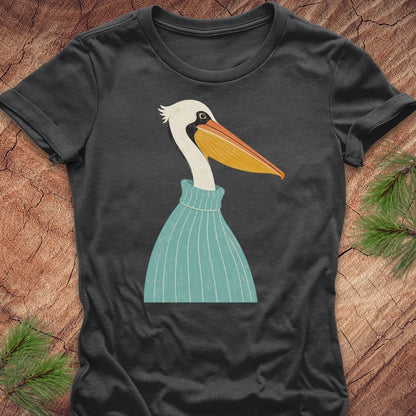 A dark charcoal gray t-shirt featuring a stylized graphic of a white pelican wearing a teal sweater, laid flat on a rustic wood background with pine needles in the corners.