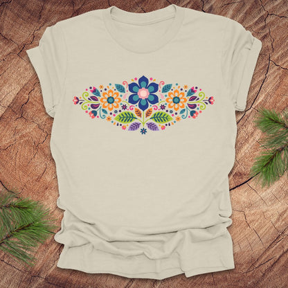 Beige t-shirt with a vibrant floral pattern in an oval shape, on a wooden background.