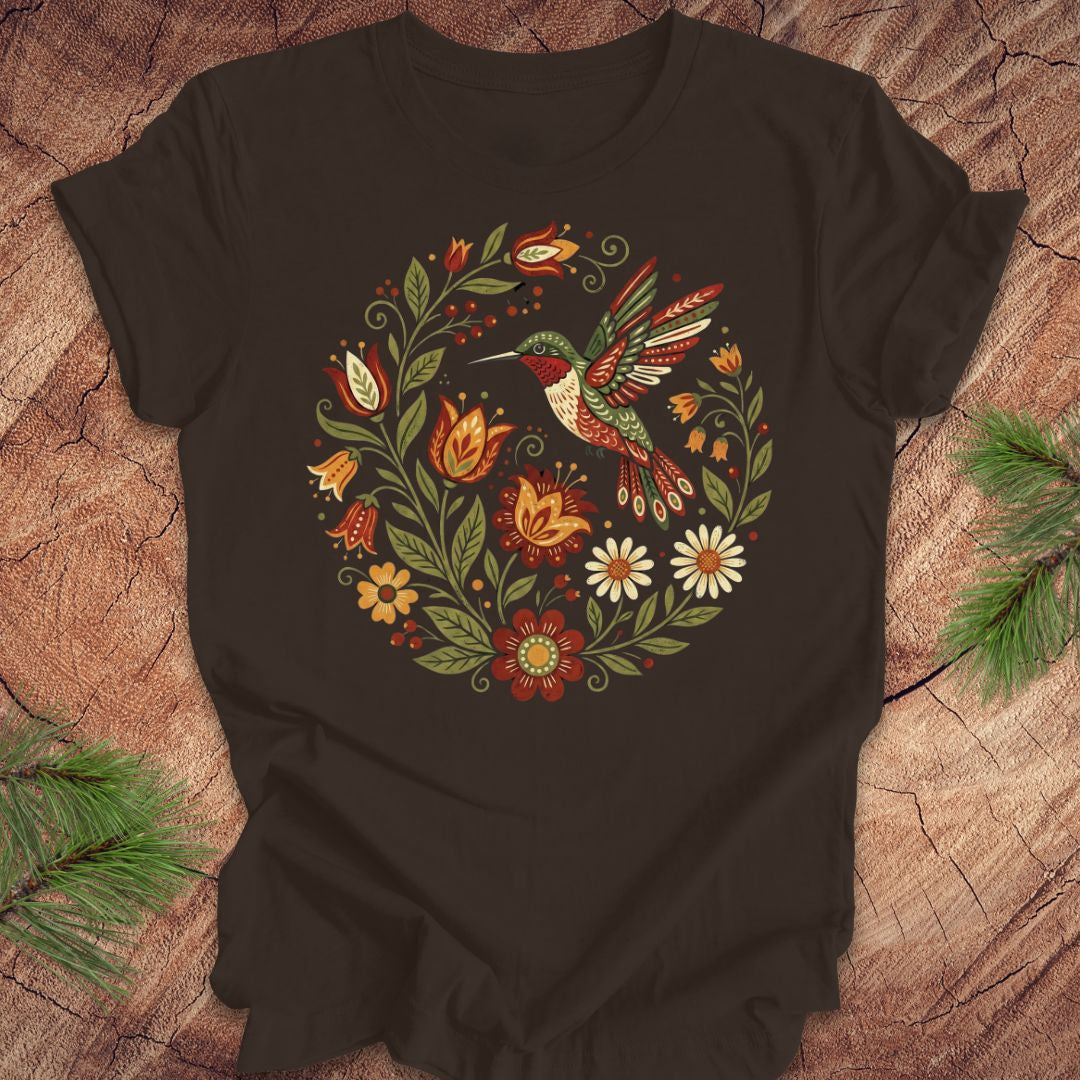 Brown t-shirt with a colorful hummingbird and floral design on a wooden surface.