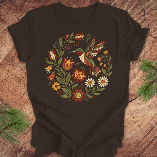Brown t-shirt with a colorful hummingbird and floral design on a wooden surface.