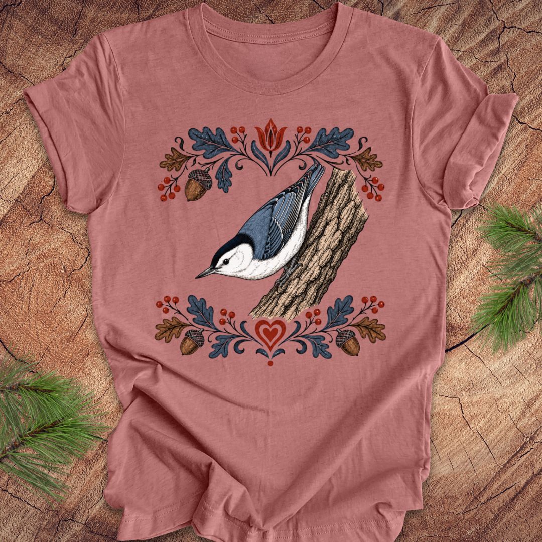 Mauve t-shirt with a nuthatch and flower design on a wooden surface