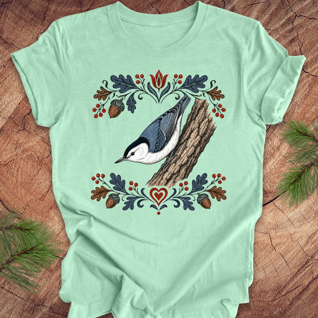 Light green t-shirt with a nuthatch and flower design on a wooden surface