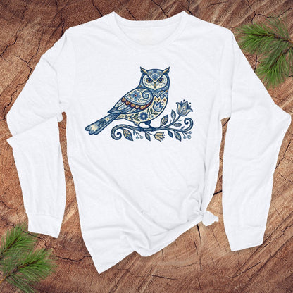 White long-sleeve shirt with a blue folk art floral owl design on a wooden surface.