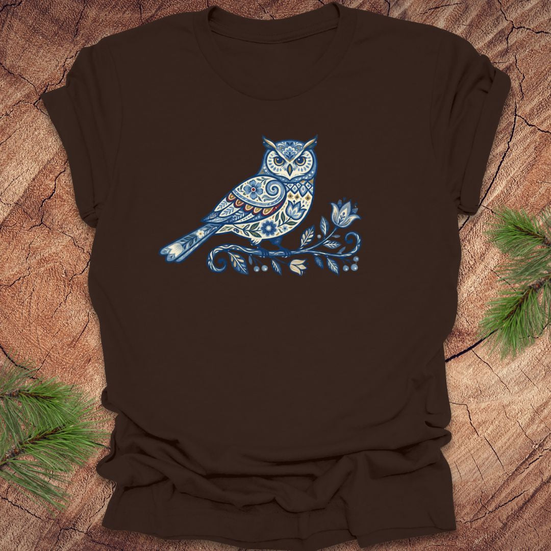 Brown t-shirt with a blue folk art floral owl design on a wooden surface