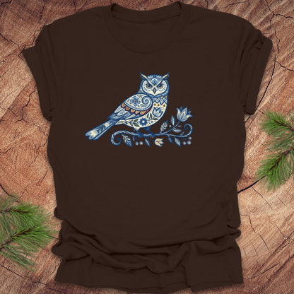 Brown t-shirt with a blue folk art floral owl design on a wooden surface