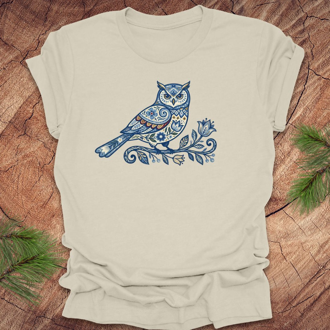 Beige t-shirt with a blue folk art floral owl design on a wooden surface
