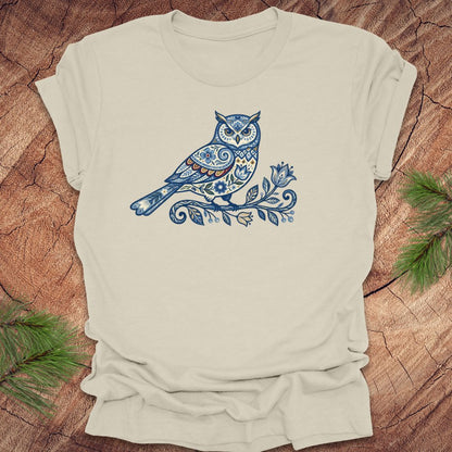 Beige t-shirt with a blue folk art floral owl design on a wooden surface