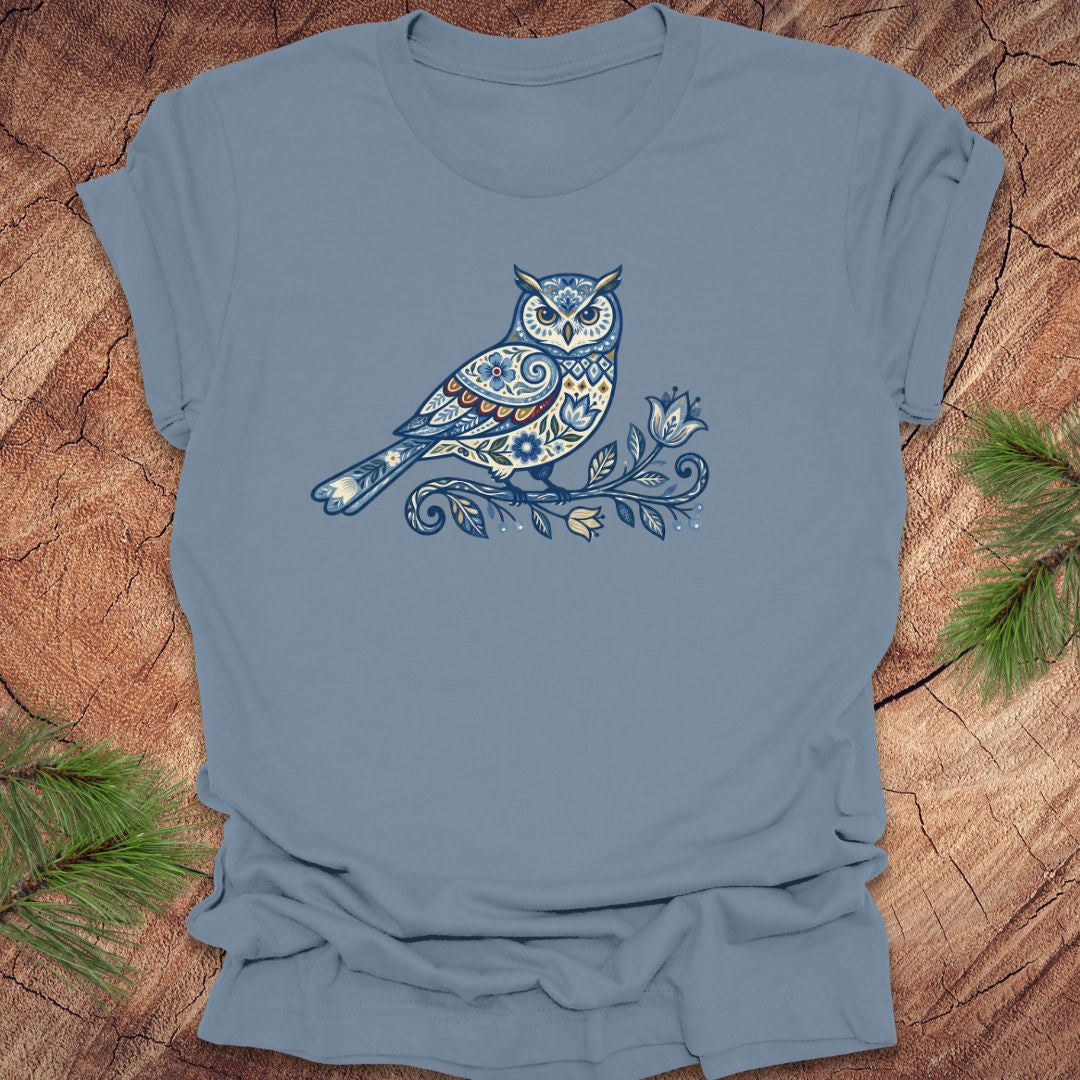 Steel blue t-shirt with a blue folk art floral owl design on a wooden surface