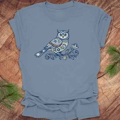 Steel blue t-shirt with a blue folk art floral owl design on a wooden surface