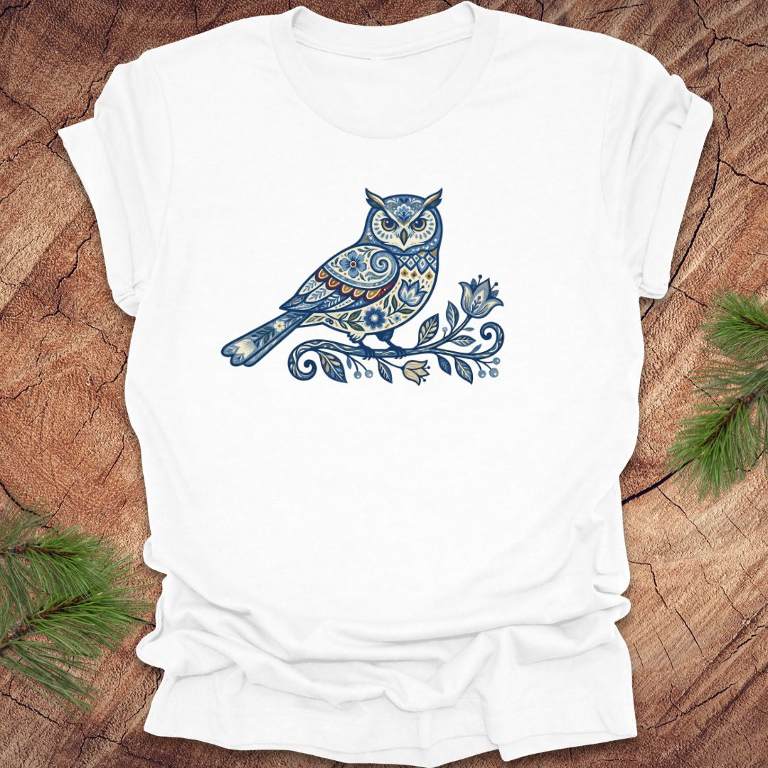 White t-shirt with a blue folk art floral owl design on a wooden surface