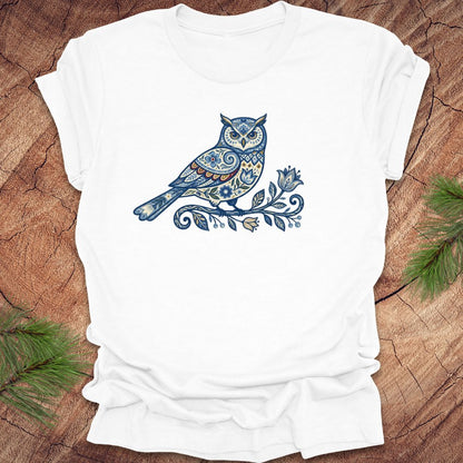 White t-shirt with a blue folk art floral owl design on a wooden surface