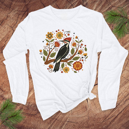 White long sleeve t-Shirt with a pileated woodpecker on a branch surrounded by folk art flowers on a wood background.
