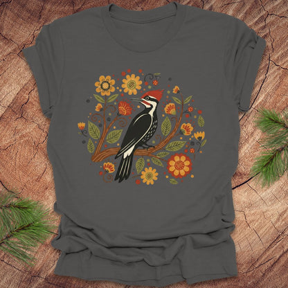 Dak gray T-Shirt with a pileated woodpecker on a branch surrounded by folk art flowers on a wood background.