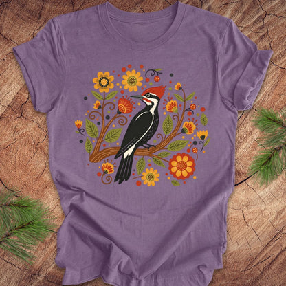 Purple t-shirt with a woodpecker and floral design on a wooden surface