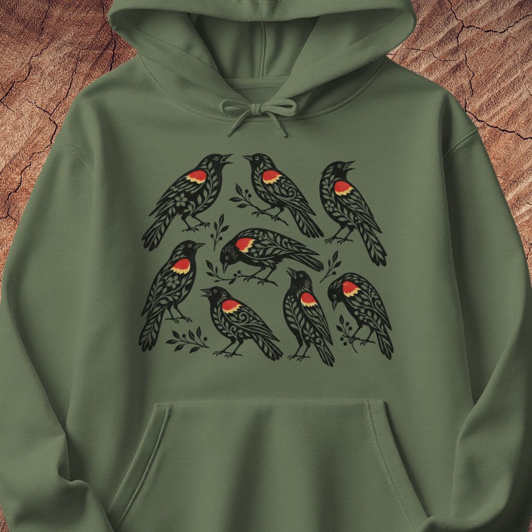 An green hoodie featuring a graphic print of eight red-winged blackbirds with red chest patches, displayed against a rustic wood background.