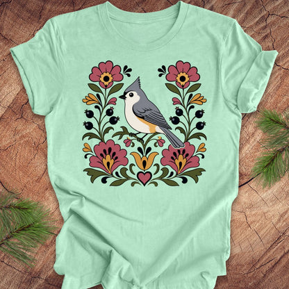 Mint green t-shirt with a titmouse and floral design on a wooden surface