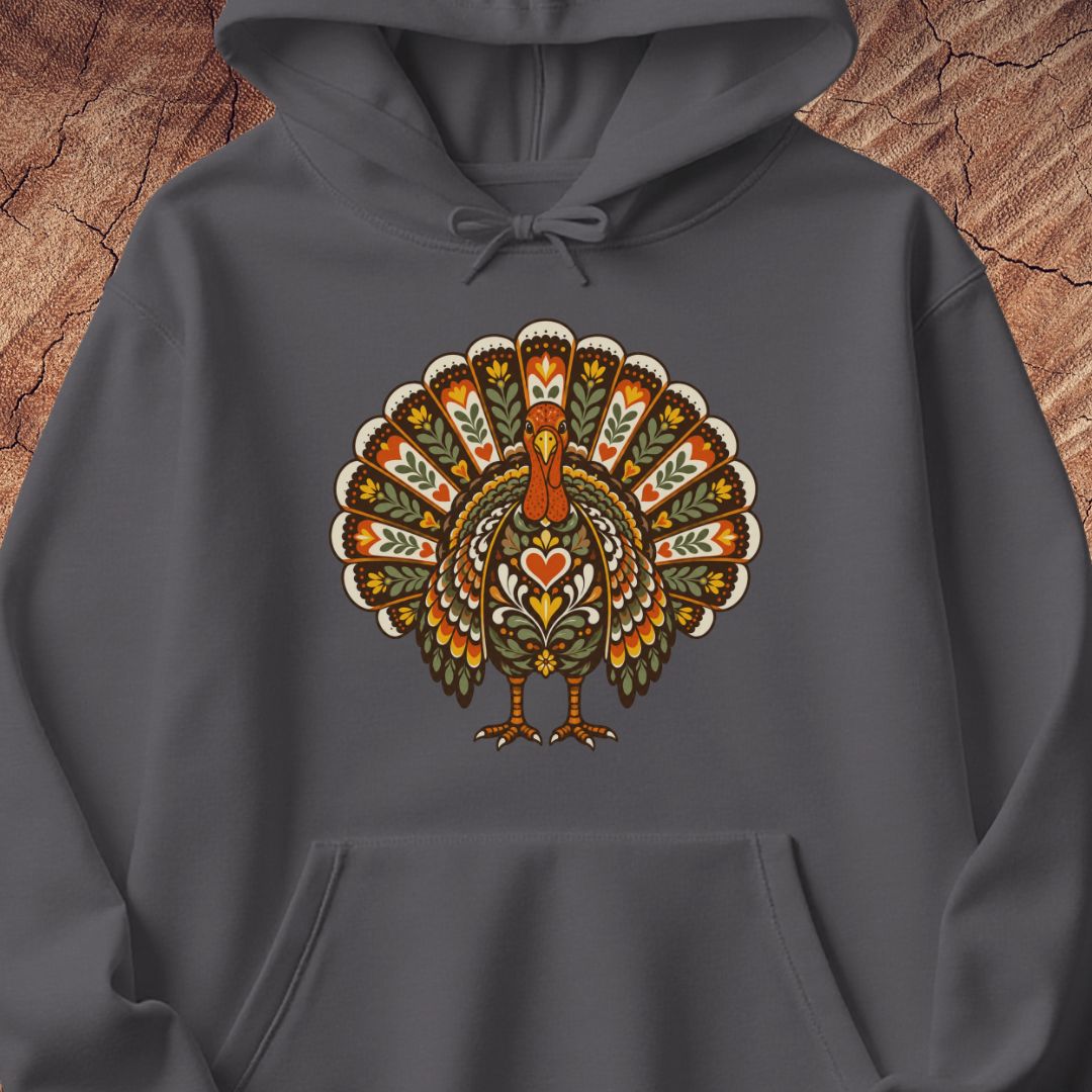 A dark gray pullover hoodie featuring a colorful, ornate turkey graphic on the chest, displayed against a rustic wood background.