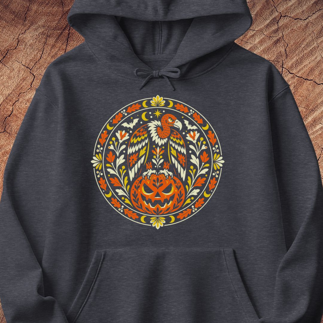 A dark heather gray hoodie featuring a large, colorful circular graphic on the chest with a stylized eagle and carved pumpkin design, displayed flat against a rustic wood background.