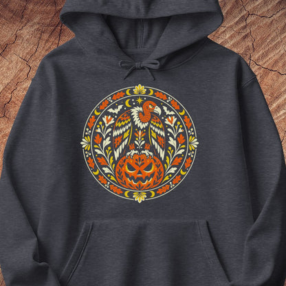 A dark heather gray hoodie featuring a large, colorful circular graphic on the chest with a stylized eagle and carved pumpkin design, displayed flat against a rustic wood background.