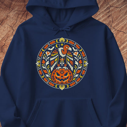 A navy blue pullover hoodie featuring a large, colorful circular graphic on the chest with a stylized eagle, pumpkin, and floral motifs in orange, yellow, white, and green, displayed against a textured brown wood background.