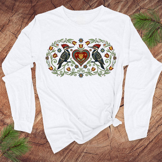 White long-sleeve shirt with a decorative design of birds and a heart on a wooden surface.