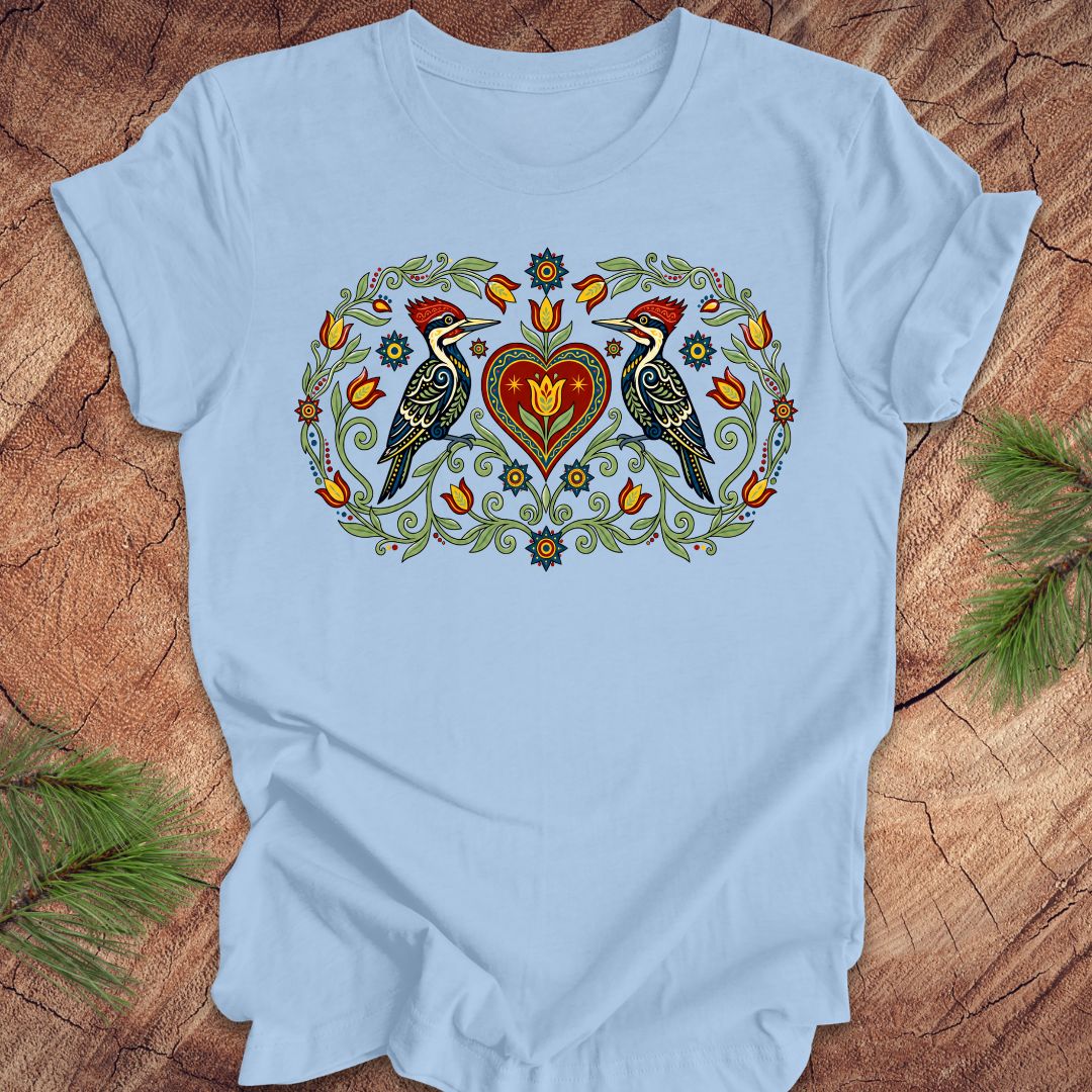 Blue t-shirt with a design of two woodpeckers around a heart on a wooden surface.