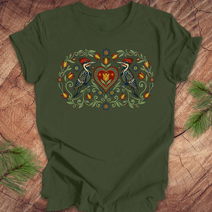 Green t-shirt with a design of two woodpeckers around a heart on a wooden surface.
