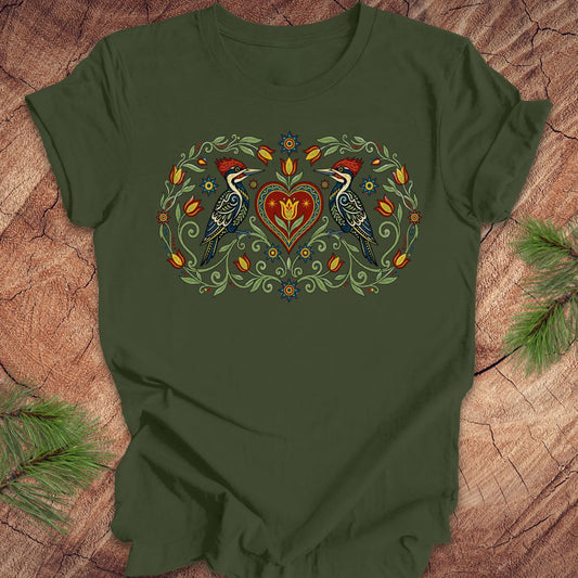 Green t-shirt with a design of two woodpeckers around a heart on a wooden surface.