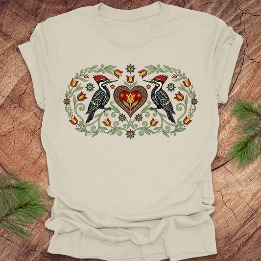 Beige t-shirt with a decorative design of two birds and a heart on a wooden surface.