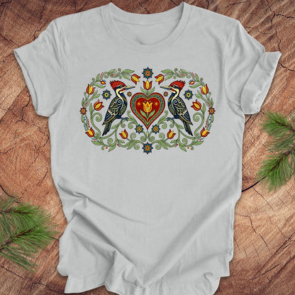 Gray t-shirt with a design of two woodpeckers around a heart on a wooden surface.