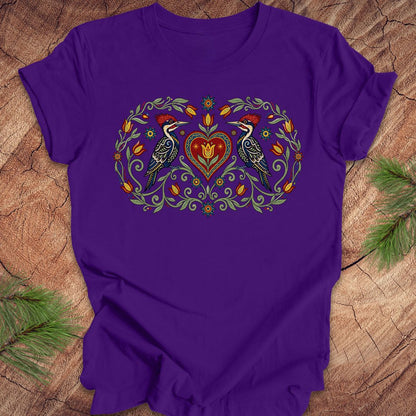 Purple t-shirt with a design of two woodpeckers around a heart on a wooden surface.