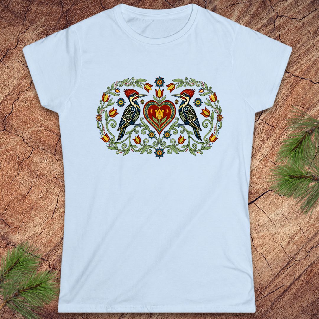 Light blue t-shirt with a decorative design featuring birds and a heart on a wooden surface.