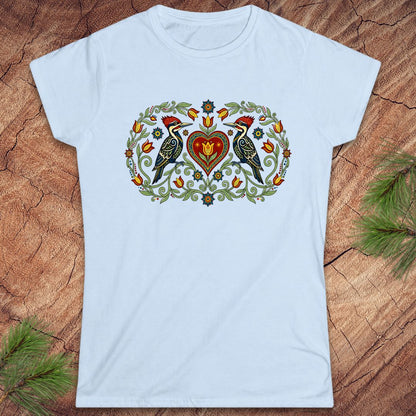 Light blue t-shirt with a decorative design featuring birds and a heart on a wooden surface.
