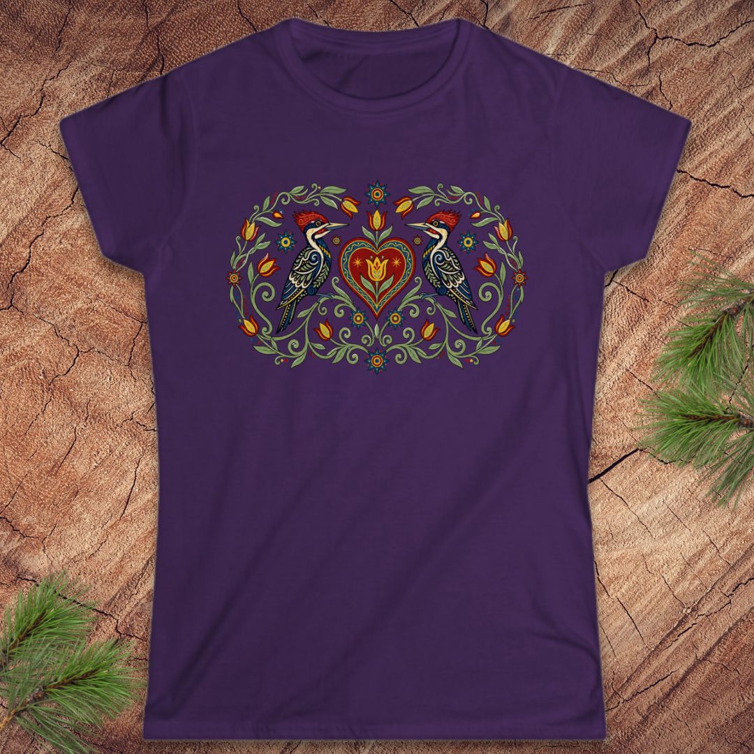 Purple t-shirt with a decorative design featuring birds and a heart on a wooden surface.