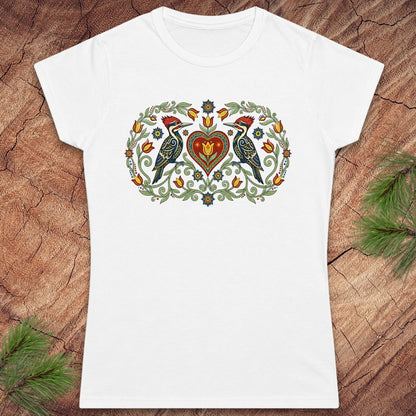 White t-shirt with a decorative design of birds and a heart on a wooden surface.
