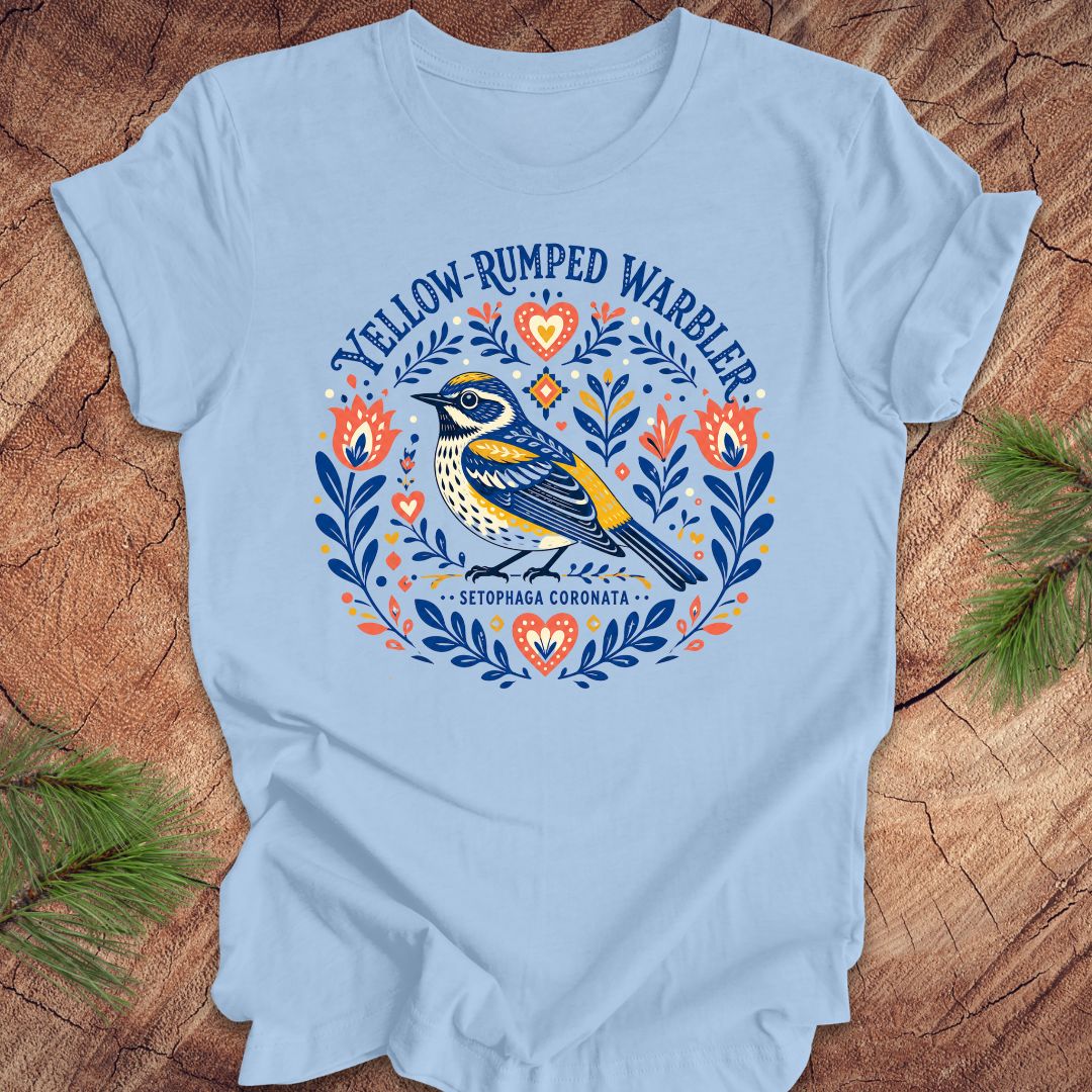 Blue t-shirt with a folk art yellow rumped warbler design on a wood background.