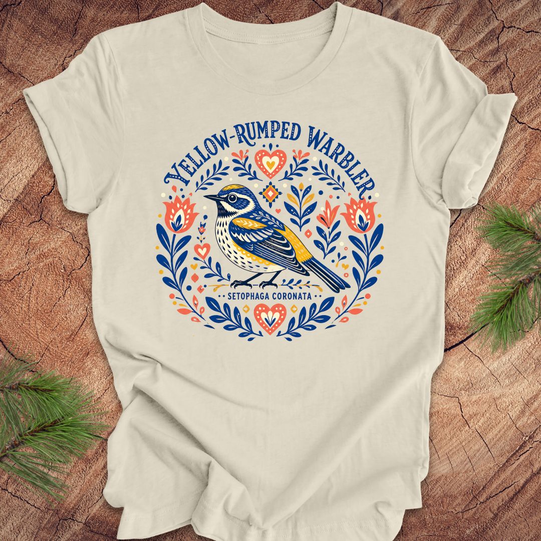 Beige t-shirt with a folk art yellow rumped warbler design on a wood background.