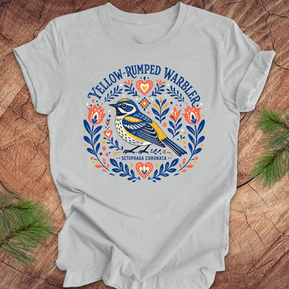 Gray t-shirt with a folk art yellow rumped warbler design on a wood background.