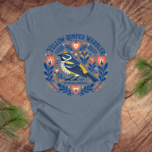 Blue t-shirt with a folk art yellow rumped warbler design on a wood background.