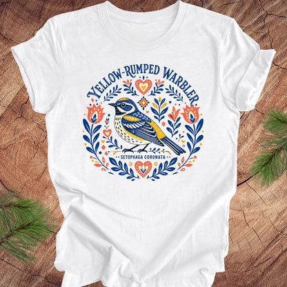 White t-shirt with a folk art yellow rumped warbler design on a wood background.