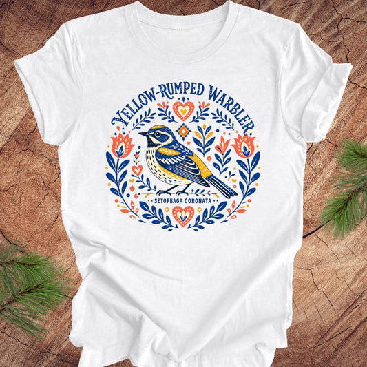 White t-shirt with a folk art yellow rumped warbler design on a wood background.